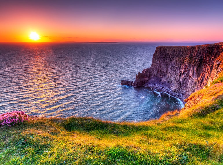 The view of a sunset behind the ocean shows a pink and purple sky