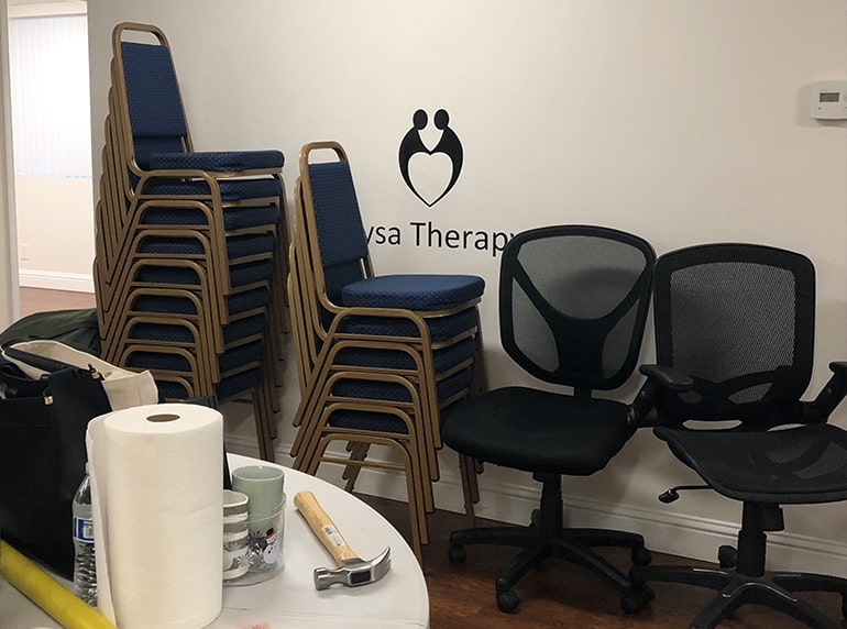 The Nysa Therapy logo is on the wall with chairs stacked in front of it.