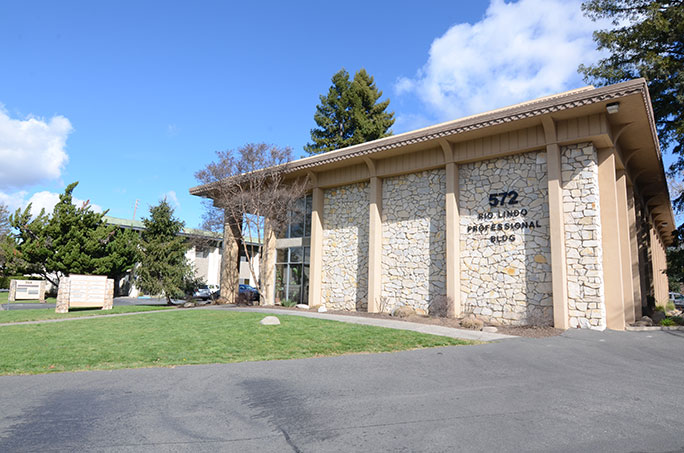 Exterior of the office building shows a patch of green grass with a stone building in the background.